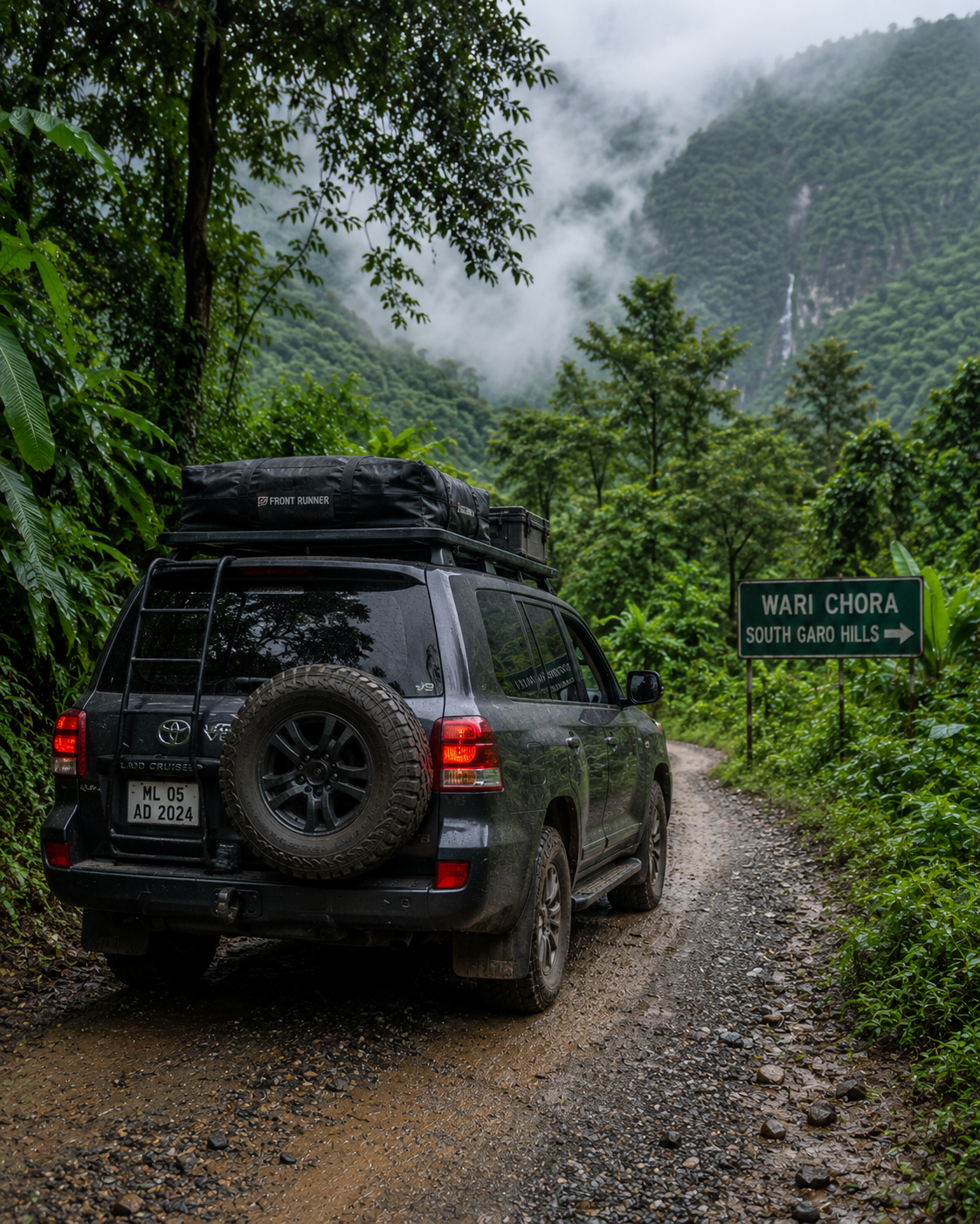 A premium 4x4 expedition vehicle driving on a remote gravel road through the lush forests of the South Garo Hills towards Wari Chora.