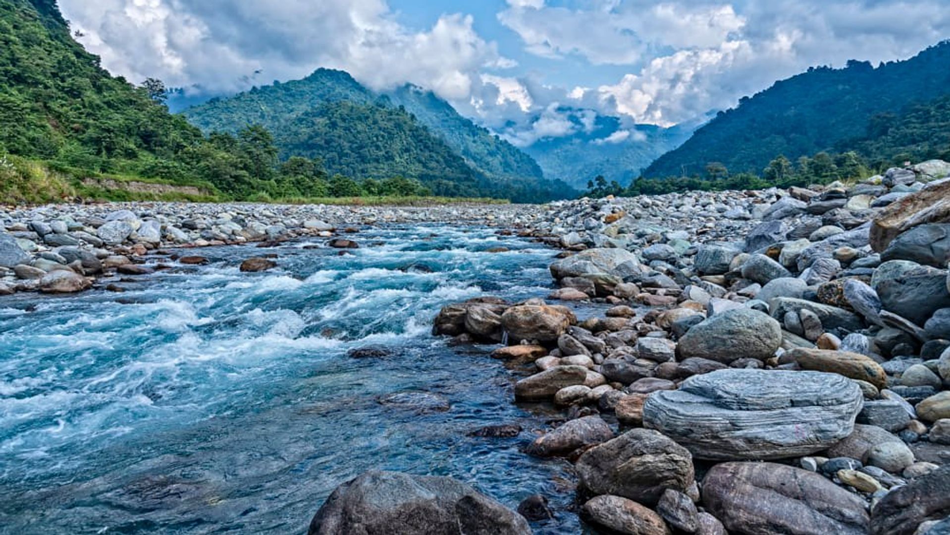 Scenic view of Roing in Arunachal Pradesh with the Dibang River flowing through rocky banks, surrounded by lush forests and misty Himalayan hills.