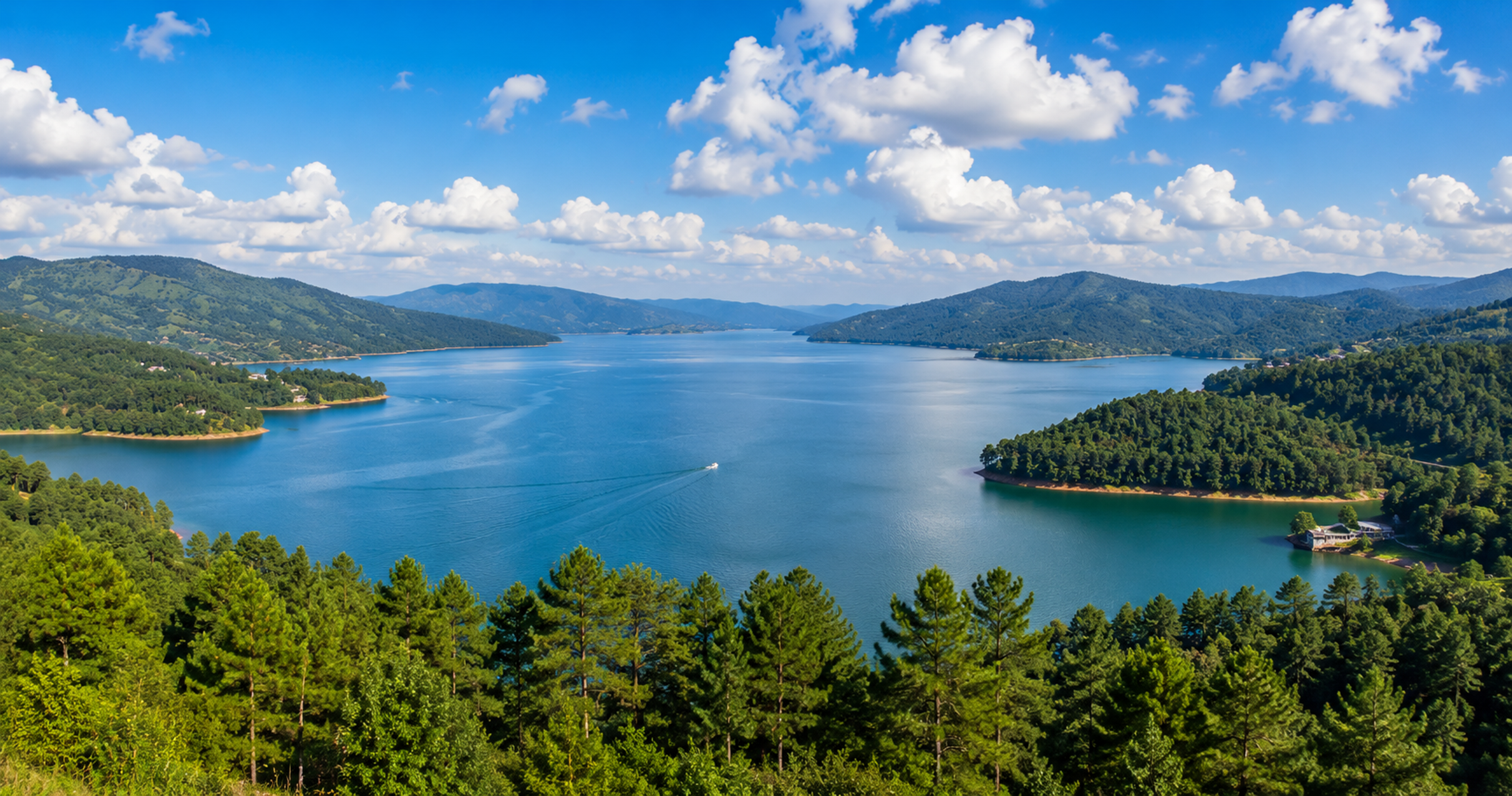 Wide panoramic view of Umiam Lake reservoir in Meghalaya flanked by dense green pine forests under a bright afternoon sky