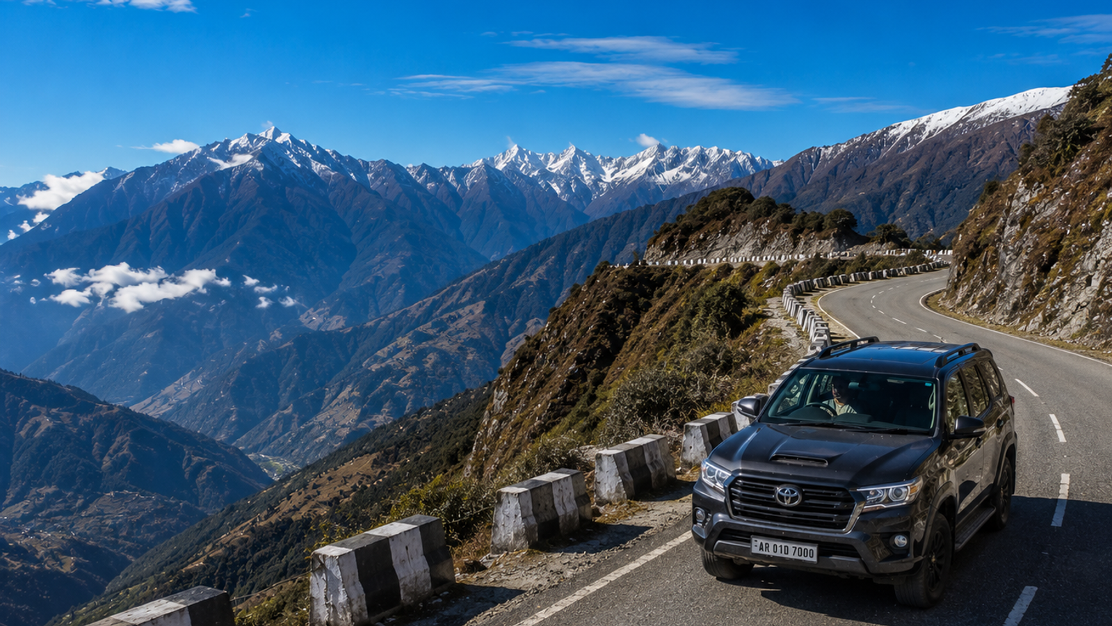 A premium 4x4 travel vehicle driving along a scenic, winding mountain highway ridge in Arunachal Pradesh under a clear blue alpine sky."