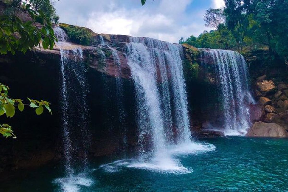 A wide shot of Krang Suri Falls showing the turquoise water and the stone path