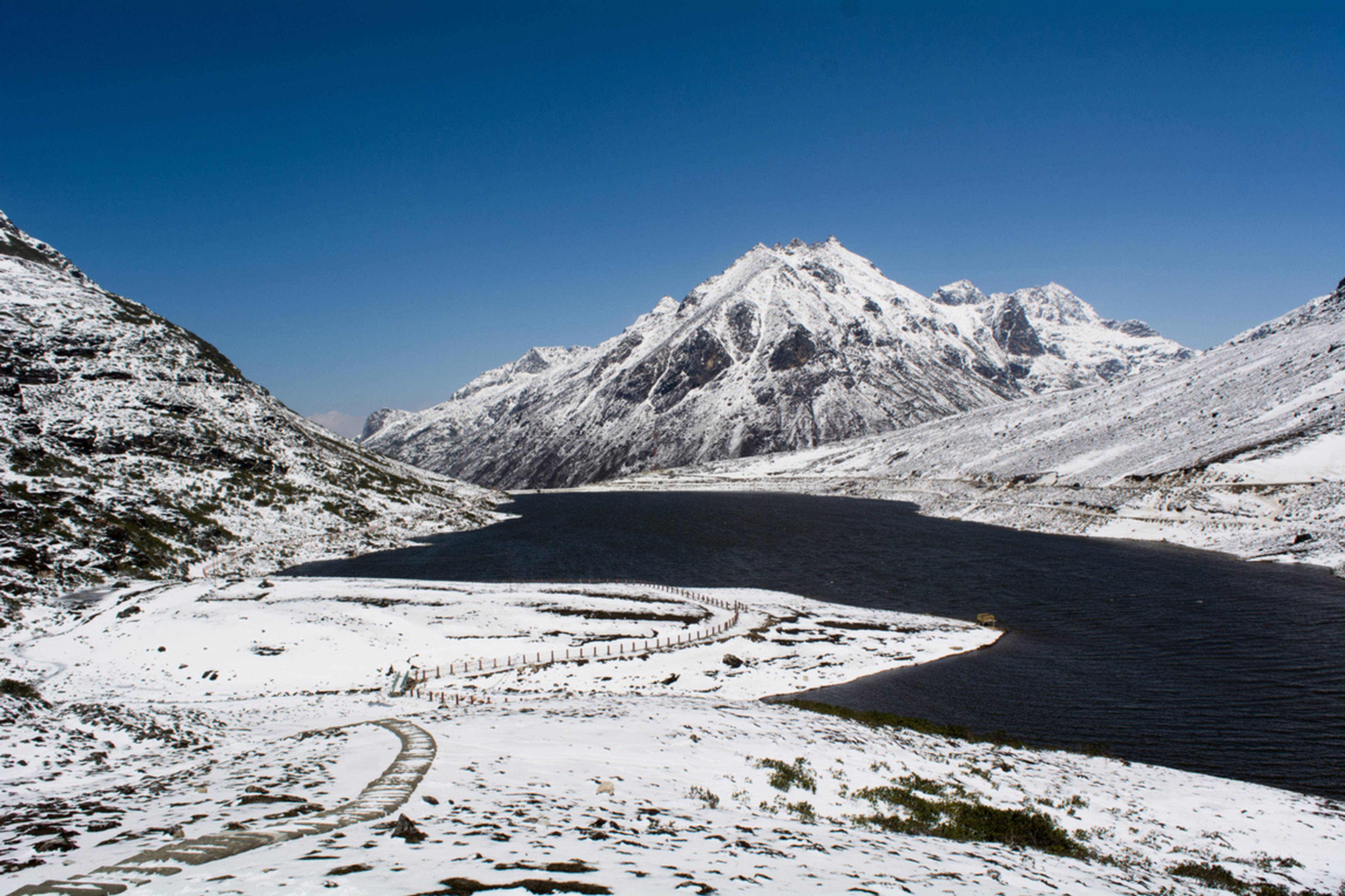 A wide view of the frozen Sela Lake (Paradise Lake) at 13,700 feet with vibrant Buddhist prayer flags fluttering against snow-capped peaks.