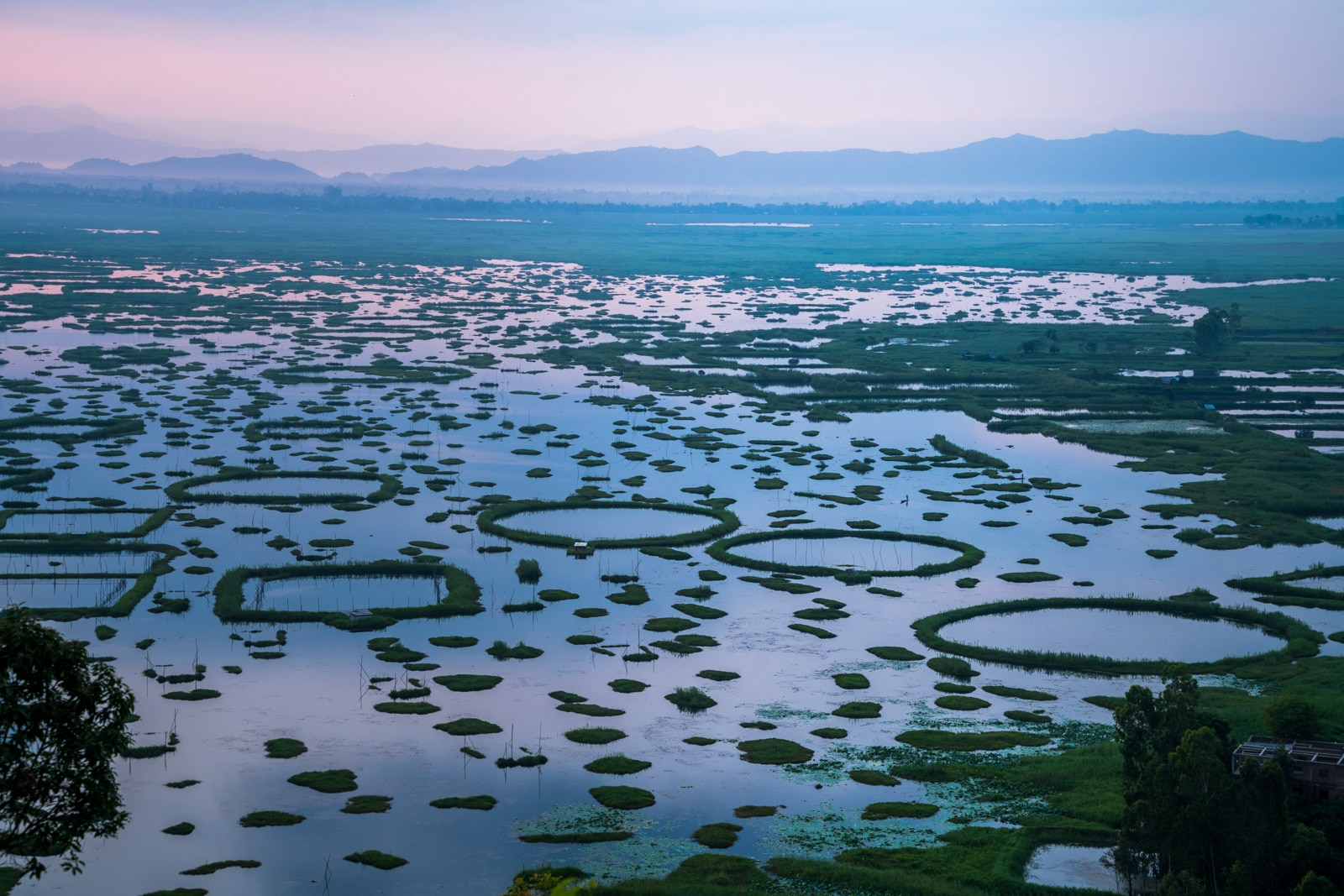 Loktak Lake Manipur – serene shoreline with rustic wooden bridge, lush green meadows and misty mountain backdrop at India's largest freshwater lake