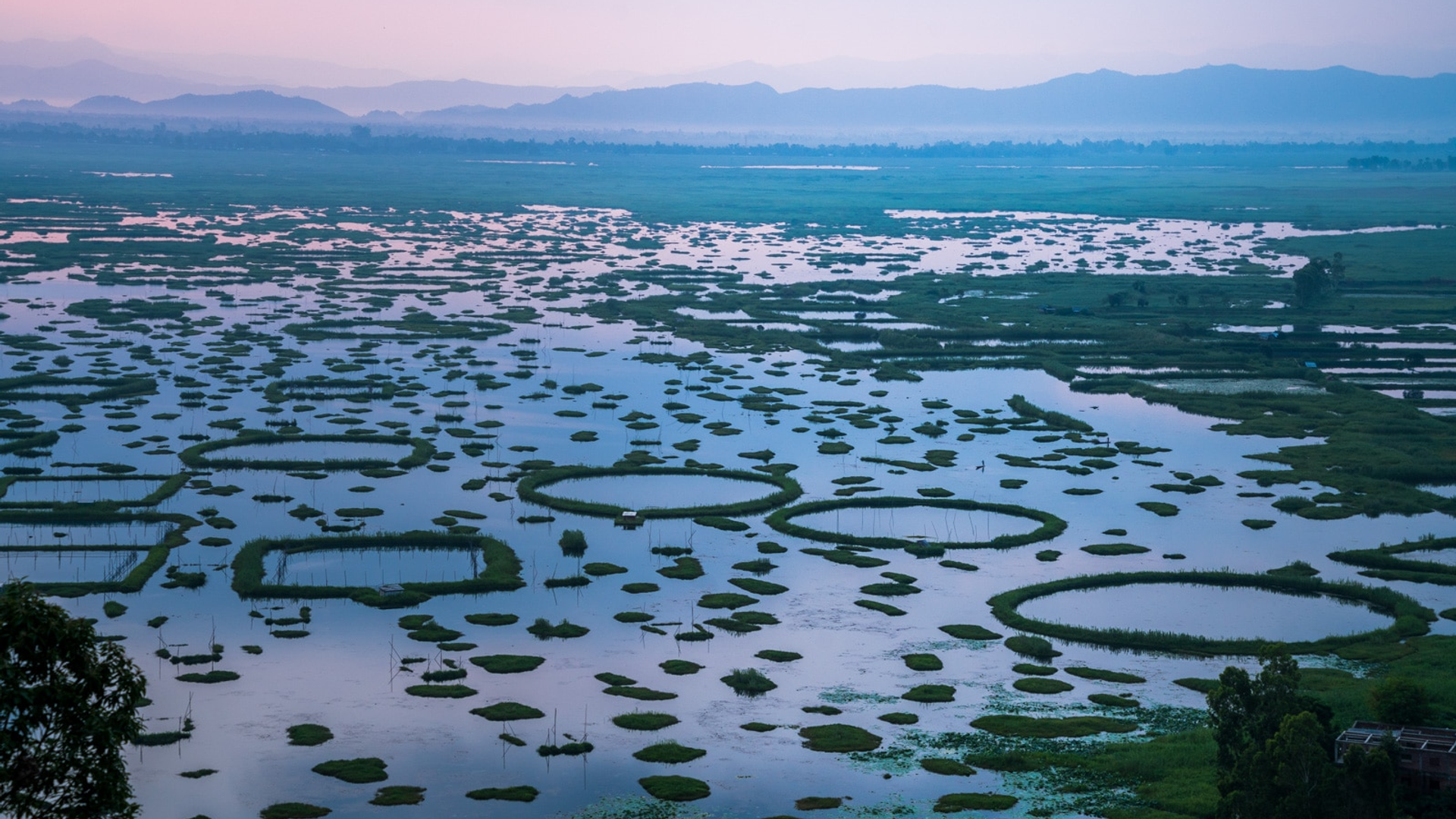 Loktak Lake Manipur – serene shoreline with rustic wooden bridge, lush green meadows and misty mountain backdrop at India's largest freshwater lake