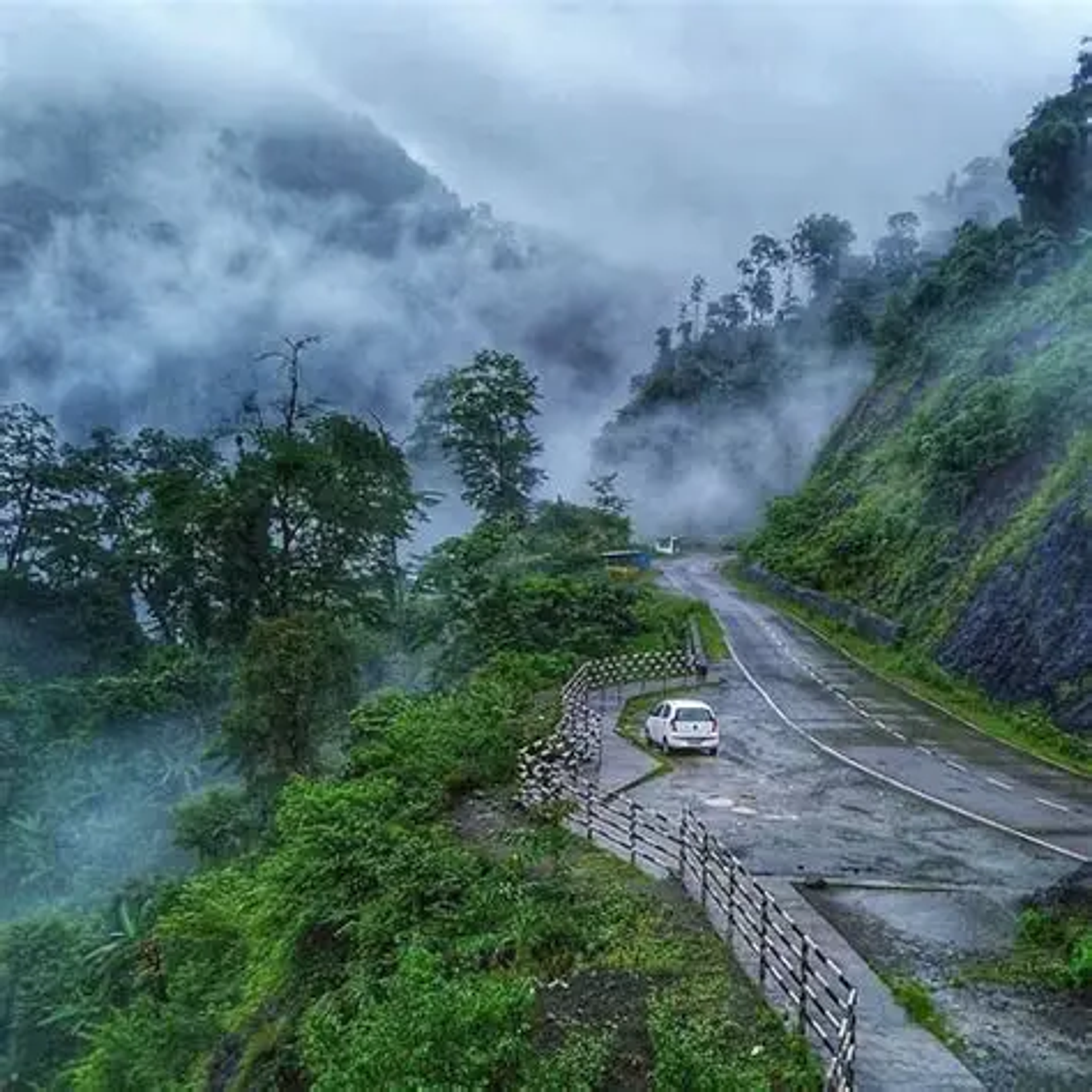  Misty mountain road with dense forest and parked car along winding curve in pasighat, Arunachal Pradesh