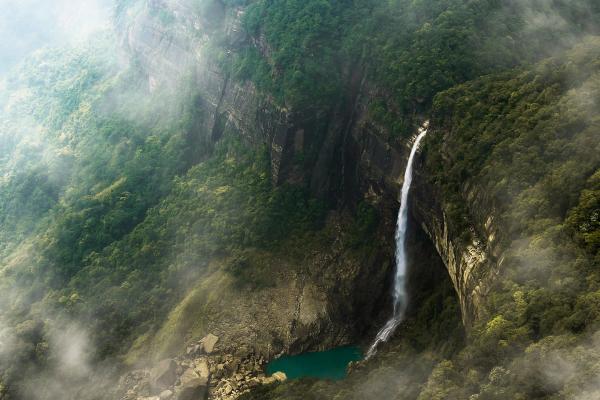 Traveler at Nohkalikai Falls Meghalaya monsoon season 2026 gear.]