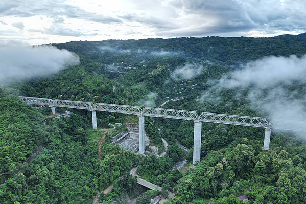 Passenger train crossing a tall concrete bridge over forested hills on the Bairabi Sairang railway line in Mizoram