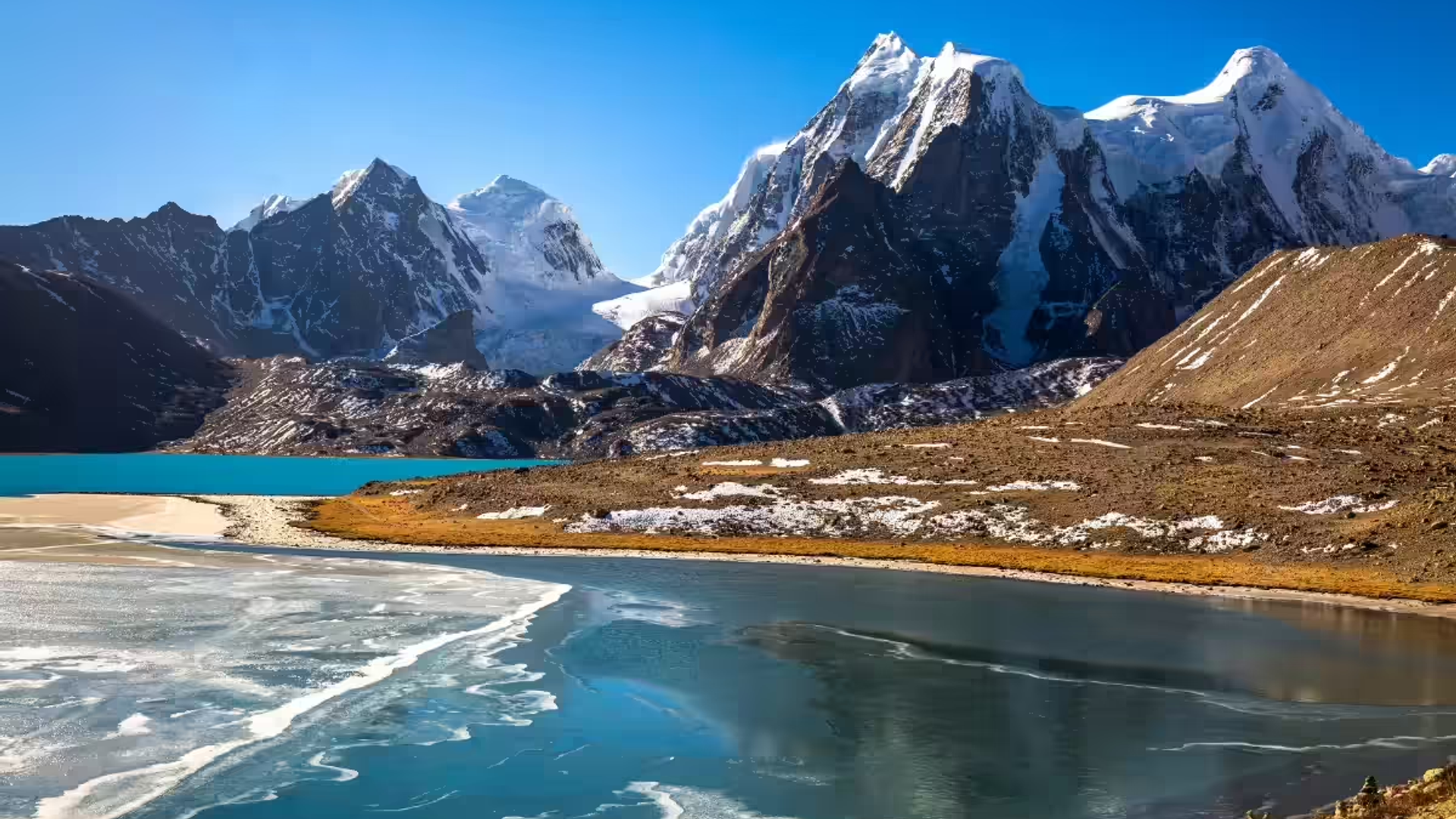 Gurudongmar Lake near Lachen in North Sikkim with crystal clear water reflecting snow-covered Himalayan mountains.
