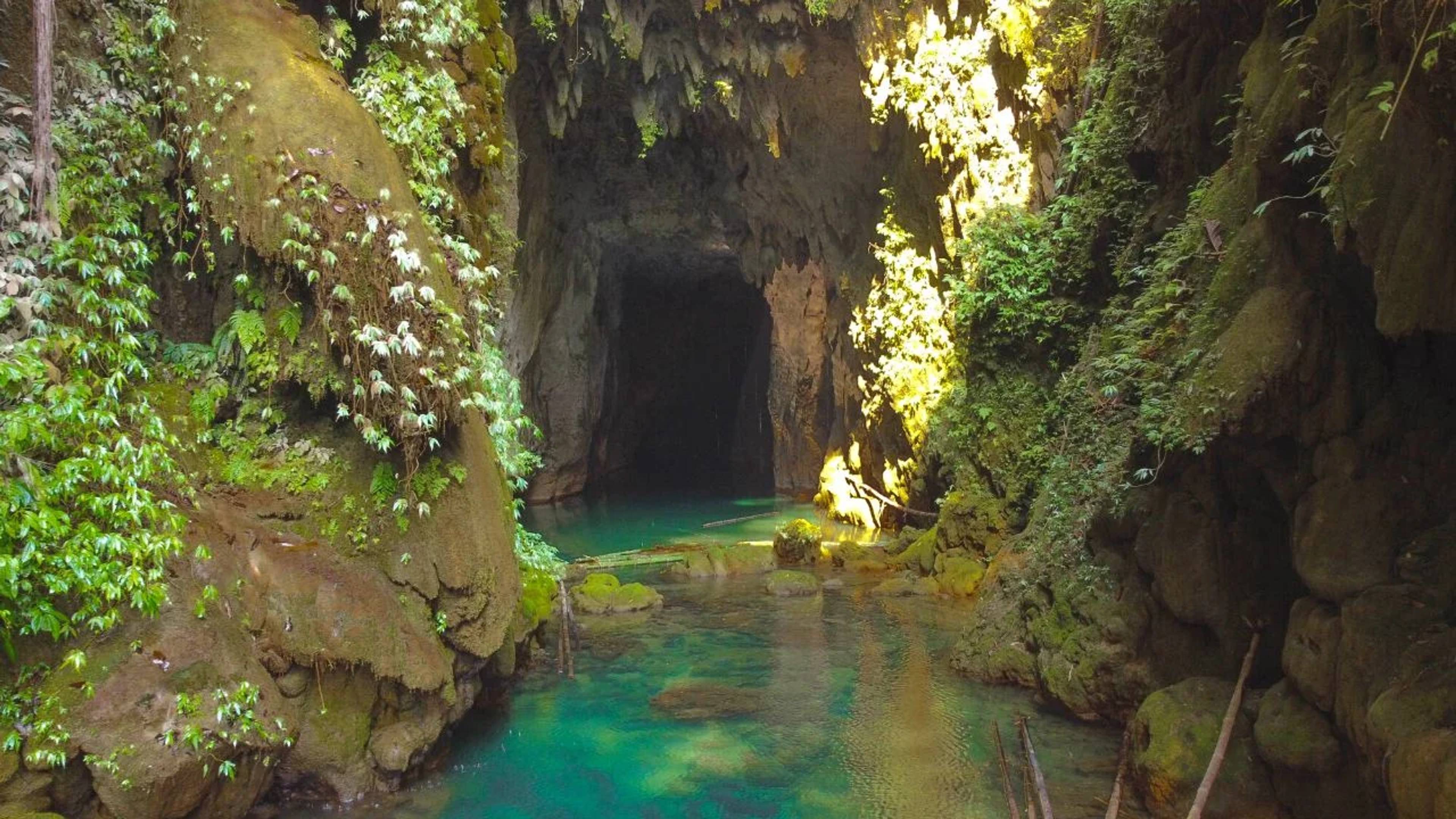Waterfall pouring from the mouth of Krem Chympe cave into a blue pool