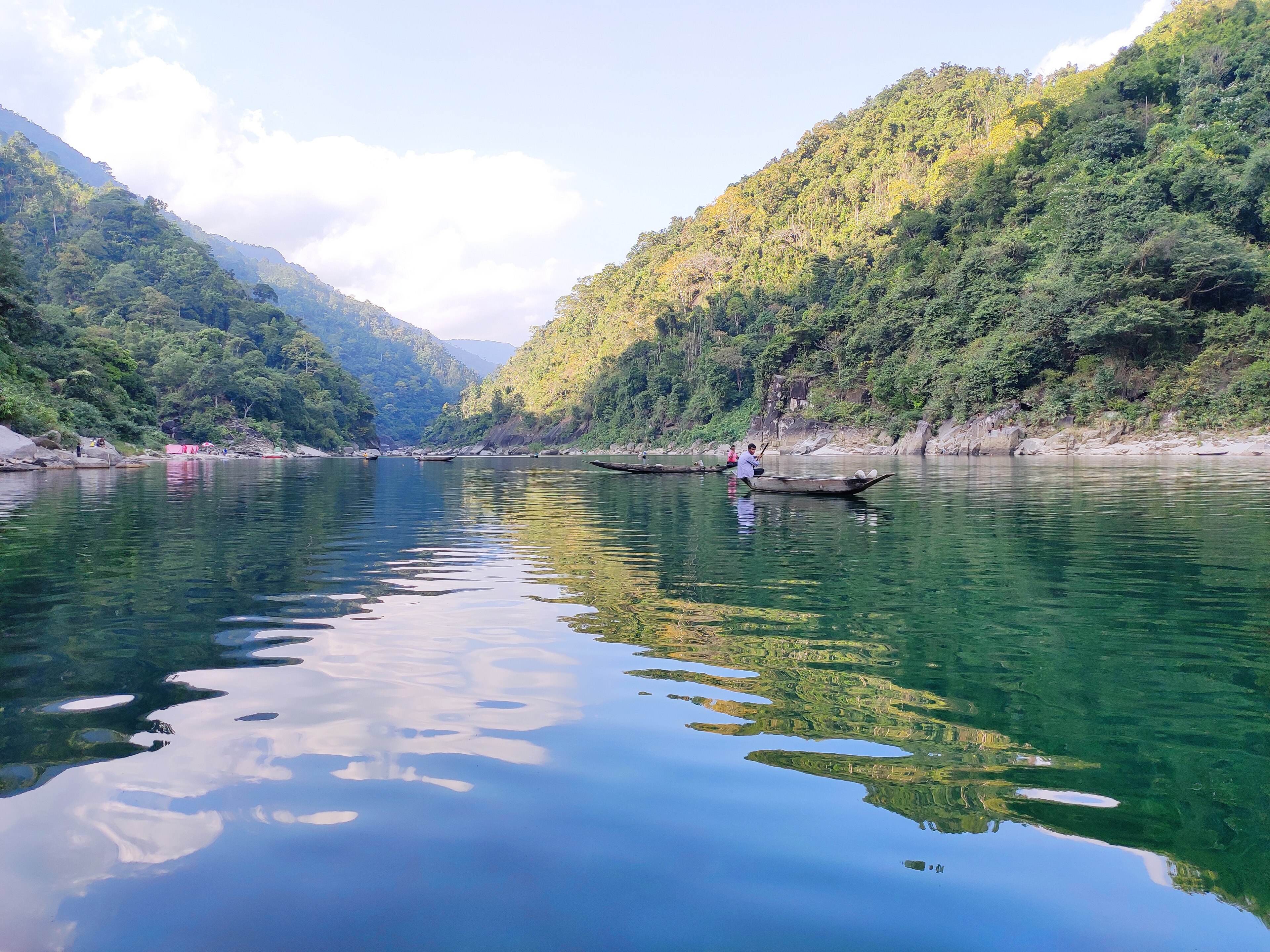 Forested hills reflected in the still Umngot river gorge