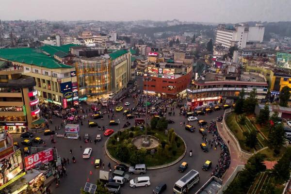 Aerial view of the Police Bazar roundabout in Shillong, Meghalaya, showing the iconic central circle and commercial buildings like the M-Crown Hotel at dusk.