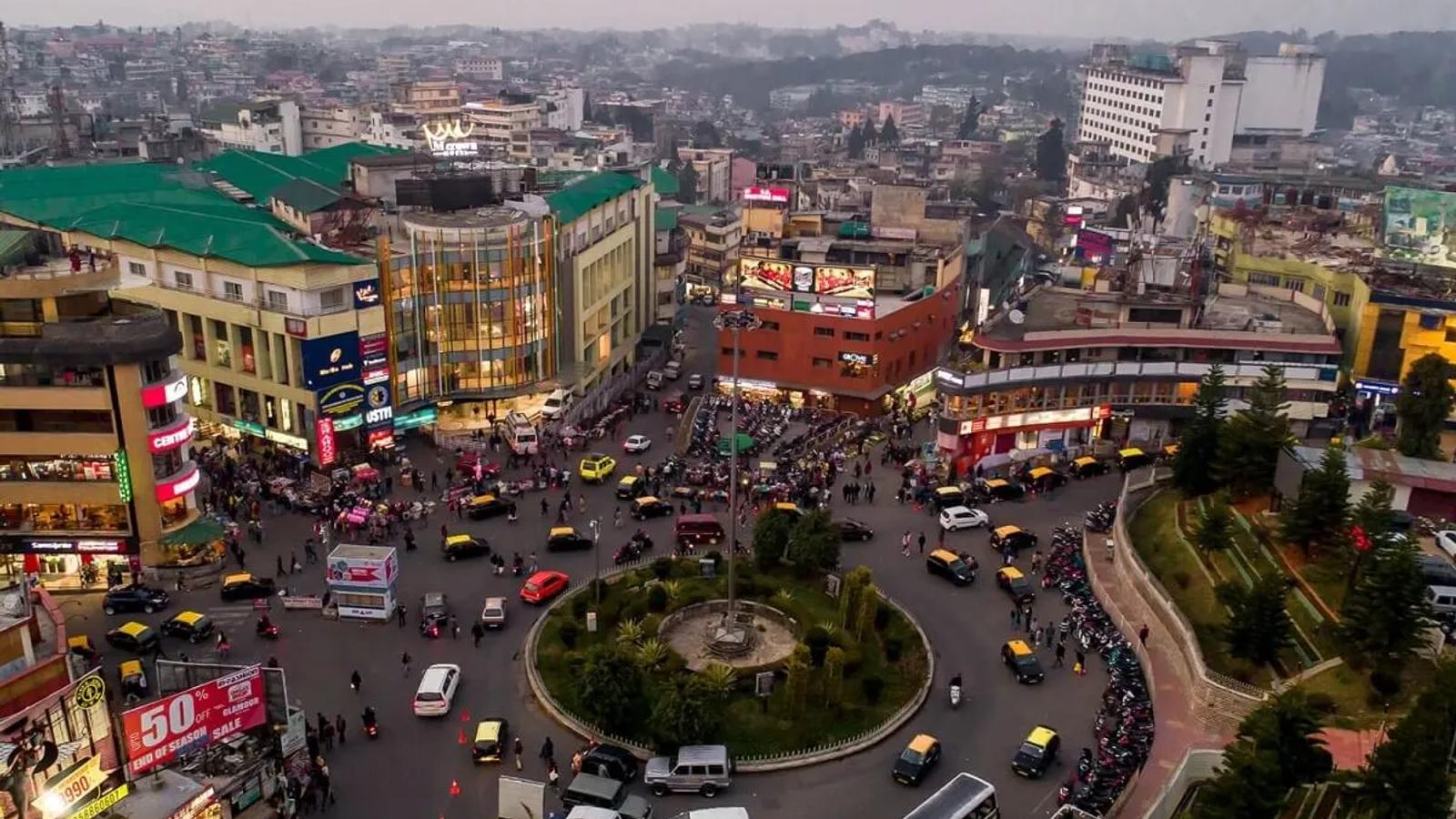 Aerial view of the Police Bazar roundabout in Shillong, Meghalaya, showing the iconic central circle and commercial buildings like the M-Crown Hotel at dusk.