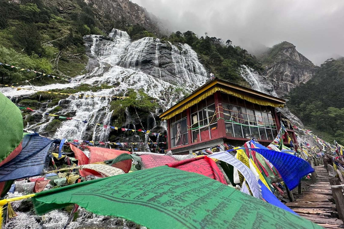 Cascading crystal-clear streams of the Chumi Gyatse Holy Waterfalls in Tawang, surrounded by colorful Buddhist prayer flags.