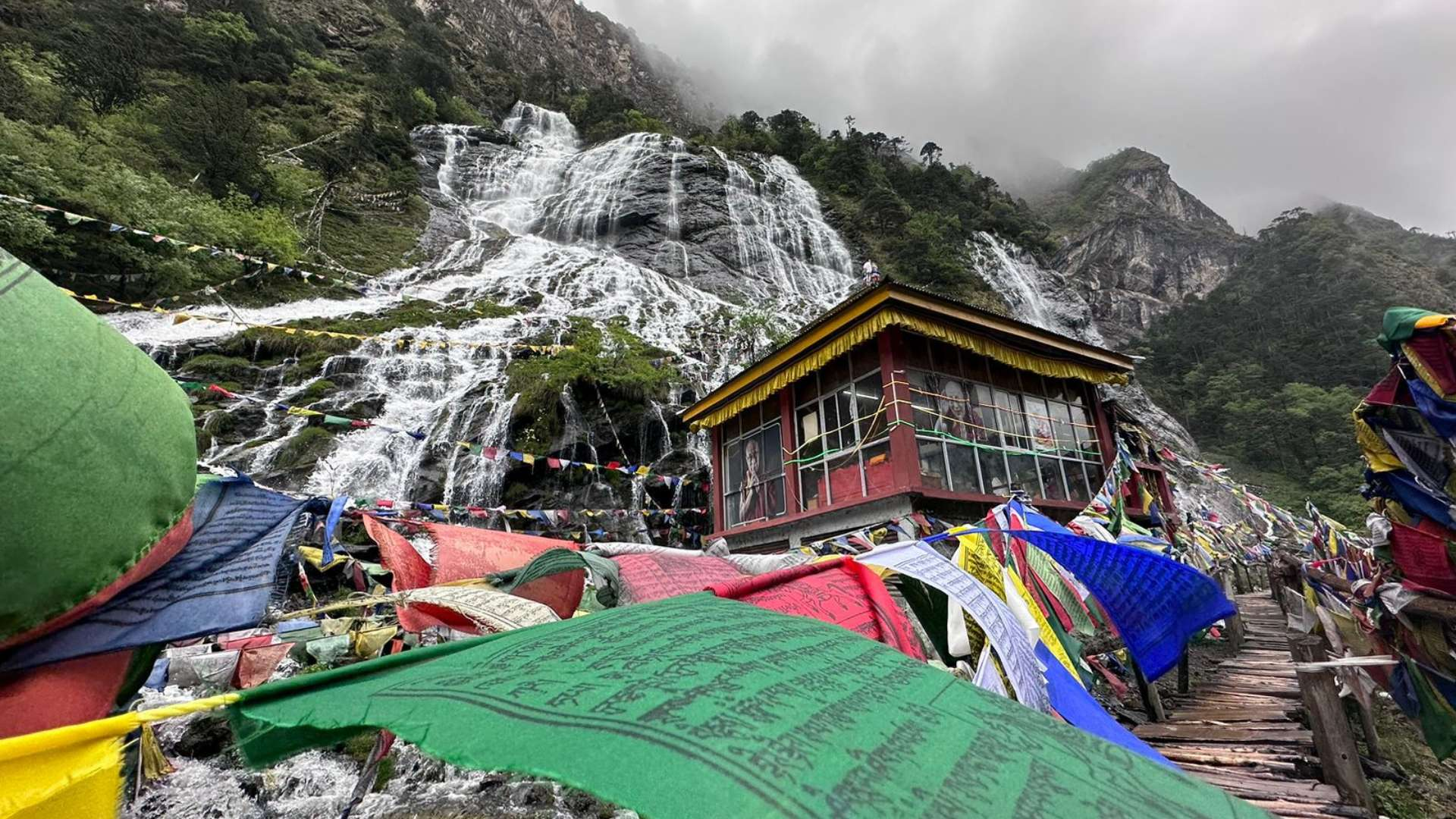 Cascading crystal-clear streams of the Chumi Gyatse Holy Waterfalls in Tawang, surrounded by colorful Buddhist prayer flags.