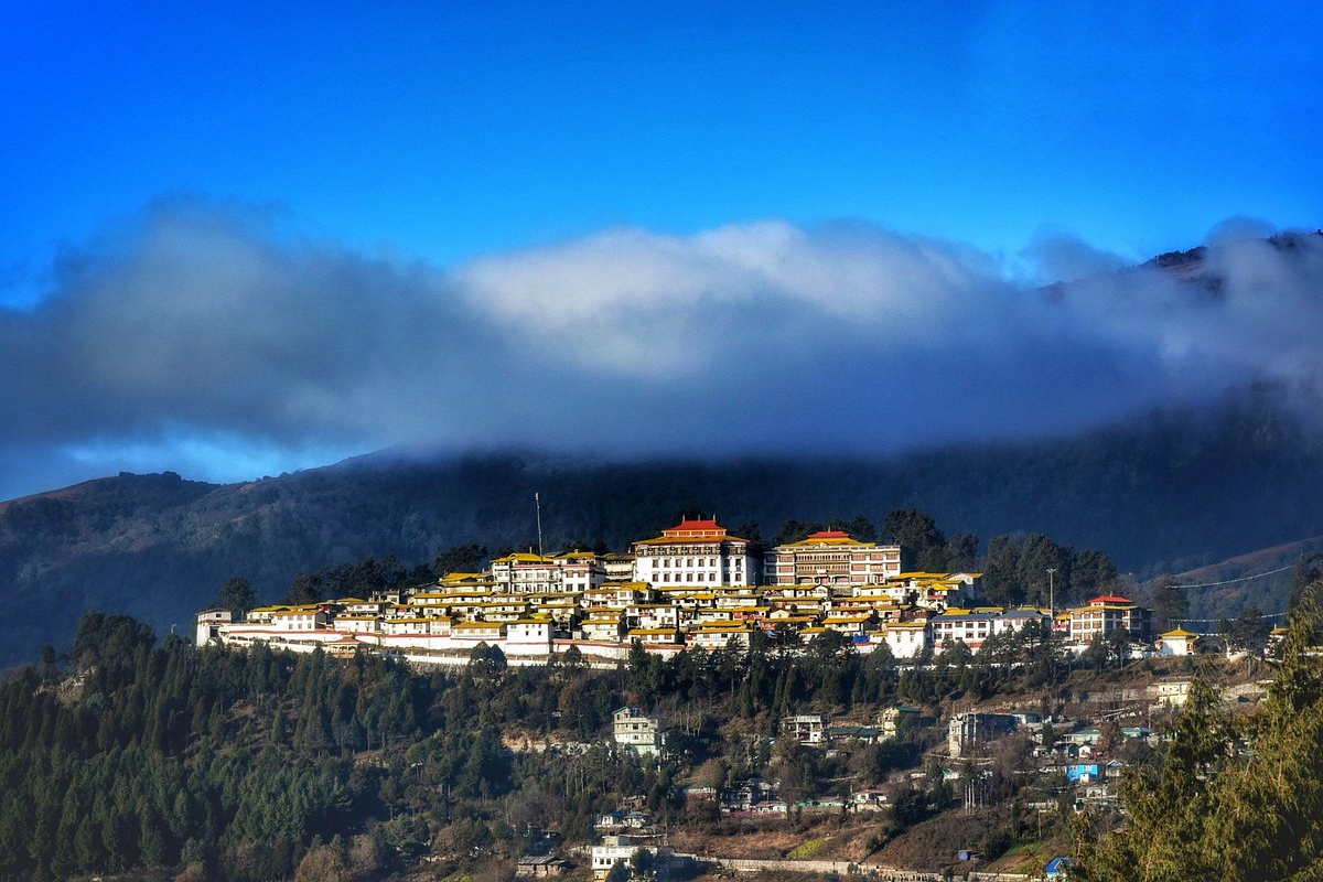 Cinematic wide shot of the yellow-roofed Tawang Monastery on a green mountain ridge under a clear blue sky.