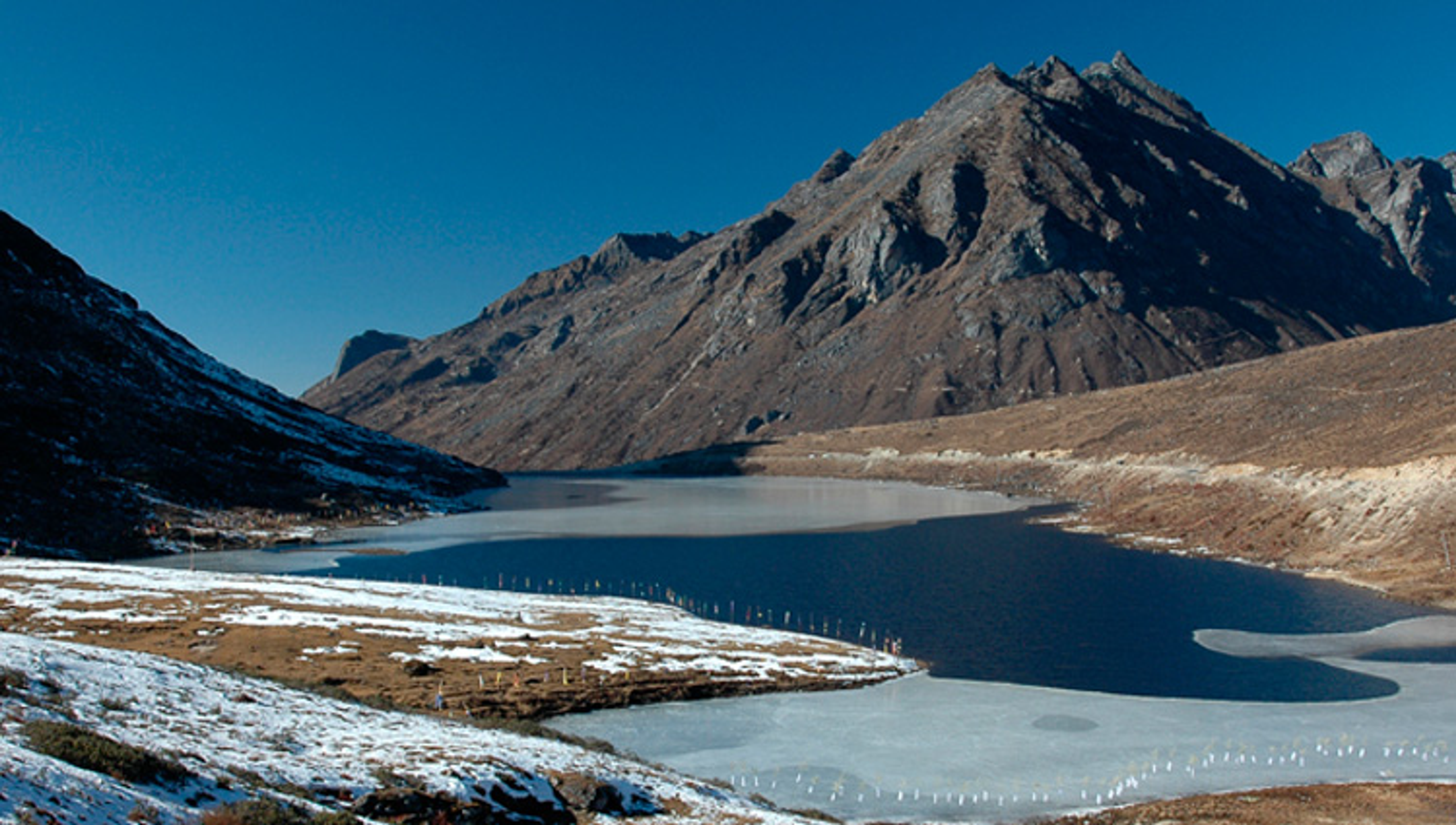 Serene landscape of P.T. Tso Lake in Tawang with snow-capped peaks reflecting in the still, high-altitude water.