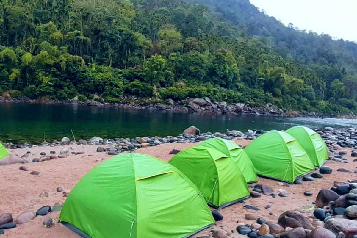Camping tents pitched along the Umngot River at Shnongpdeng with the river glowing at night and Bangladesh lights visible across the water