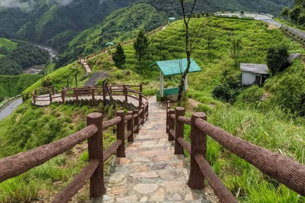 Stone path with wooden railings leading down a lush green hillside in meghalaya.