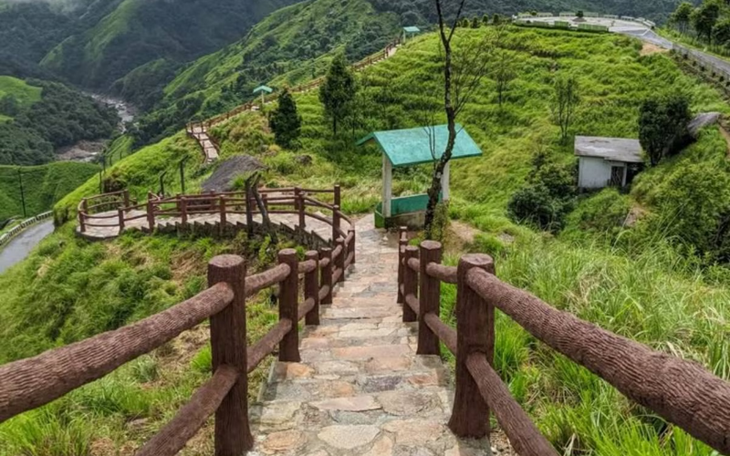 Stone path with wooden railings leading down a lush green hillside in meghalaya.