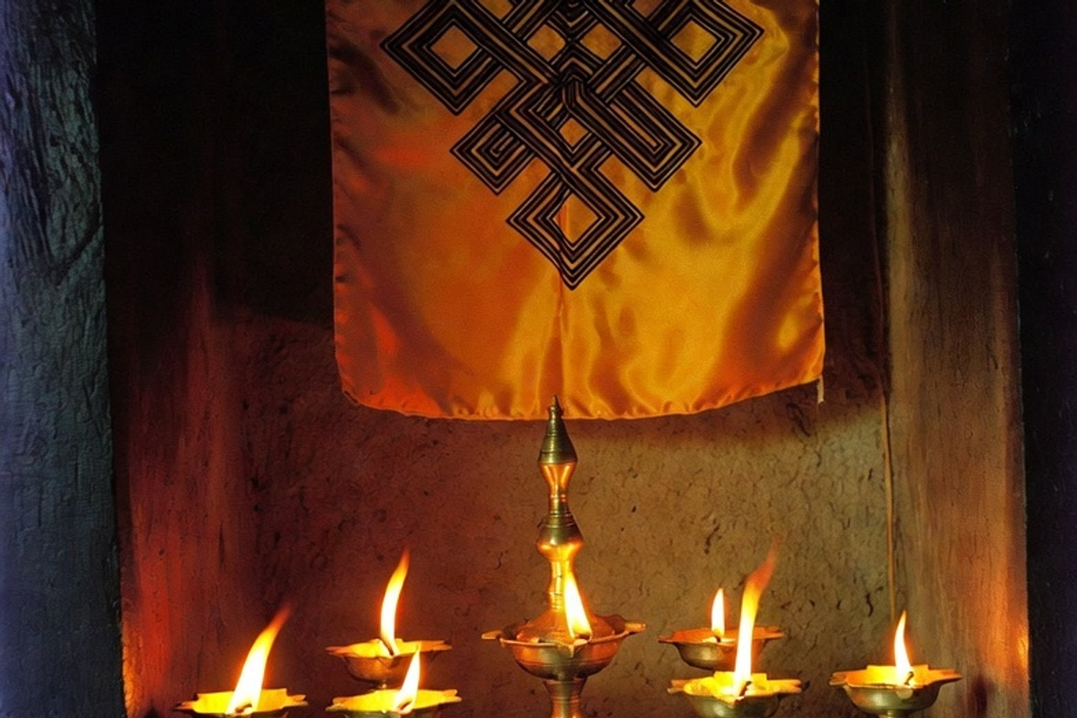 A traditional home altar in Sikkim displaying lit brass butter lamps and a silk wall-hanging of the Buddhist Endless Knot symbol.