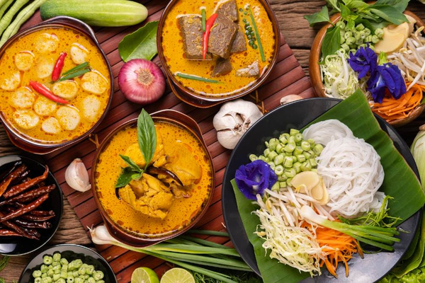 A colorful spread of traditional Meghalaya food including Jadoh, smoky Dohneiiong with black sesame, and Pukhlein rice cakes served with fresh local greens on a wooden table