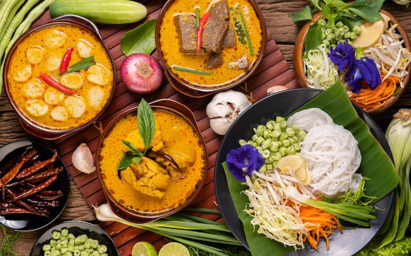 A colorful spread of traditional Meghalaya food including Jadoh, smoky Dohneiiong with black sesame, and Pukhlein rice cakes served with fresh local greens on a wooden table
