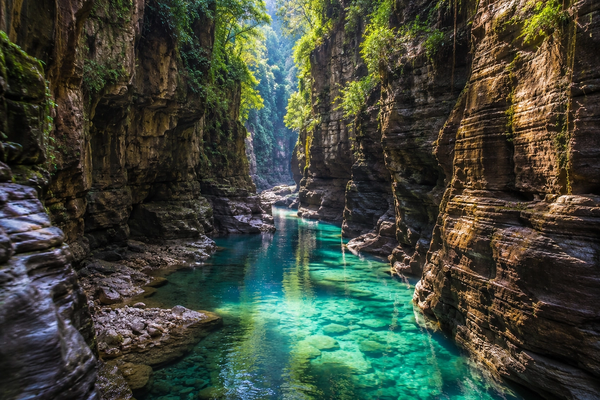 text A beautiful hidden canyon with towering vertical rock cliffs and a clear turquoise river running through it.