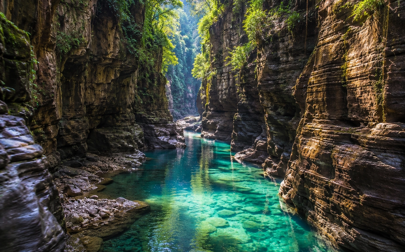 text A beautiful hidden canyon with towering vertical rock cliffs and a clear turquoise river running through it.