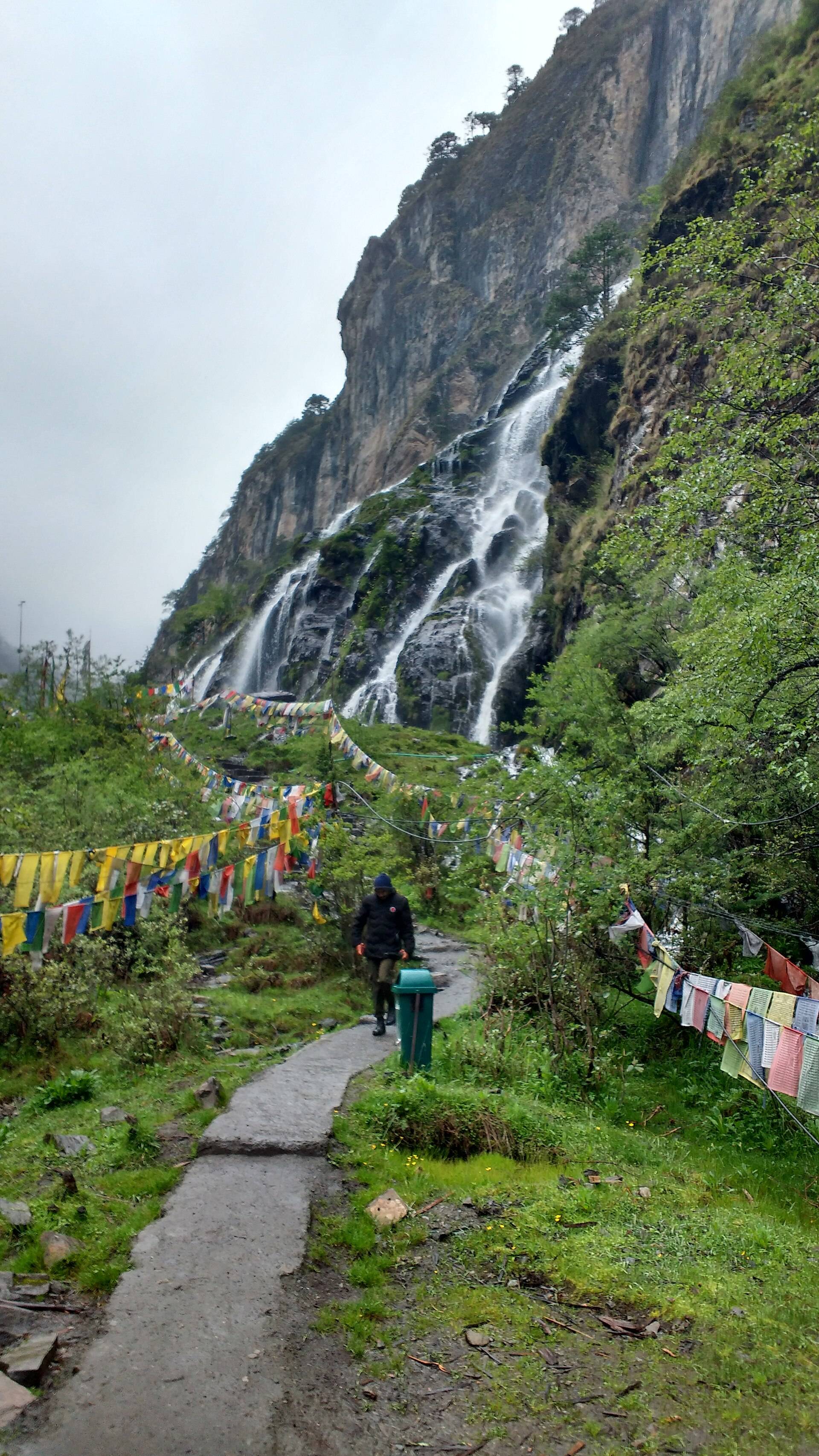 Chumi Gyatse holy waterfalls falling down a cliff with prayer flags along the path
