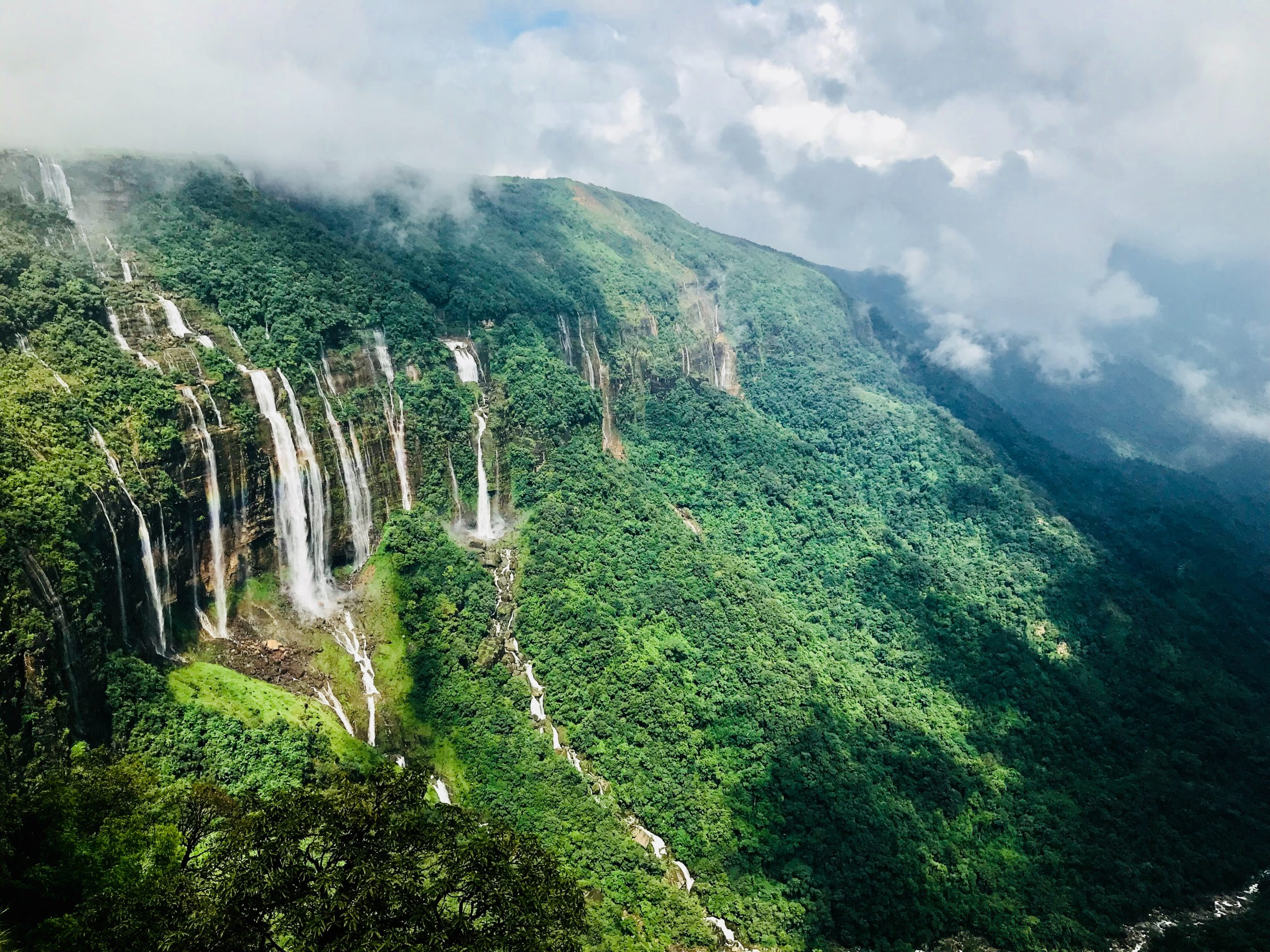 Seven parallel waterfalls cascading down a lush green cliff in meghalaya.