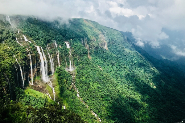 Seven parallel waterfalls cascading down a lush green cliff in meghalaya.