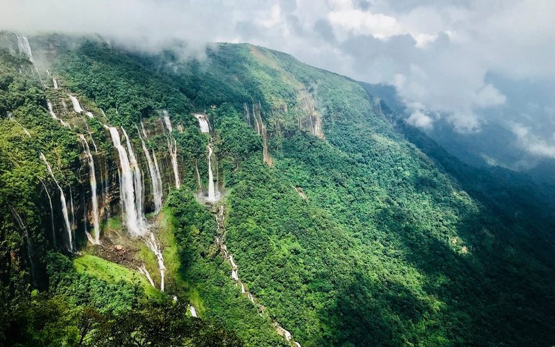 Seven parallel waterfalls cascading down a lush green cliff in meghalaya.