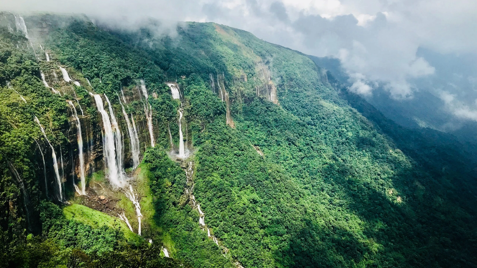 Seven parallel waterfalls cascading down a lush green cliff in meghalaya.