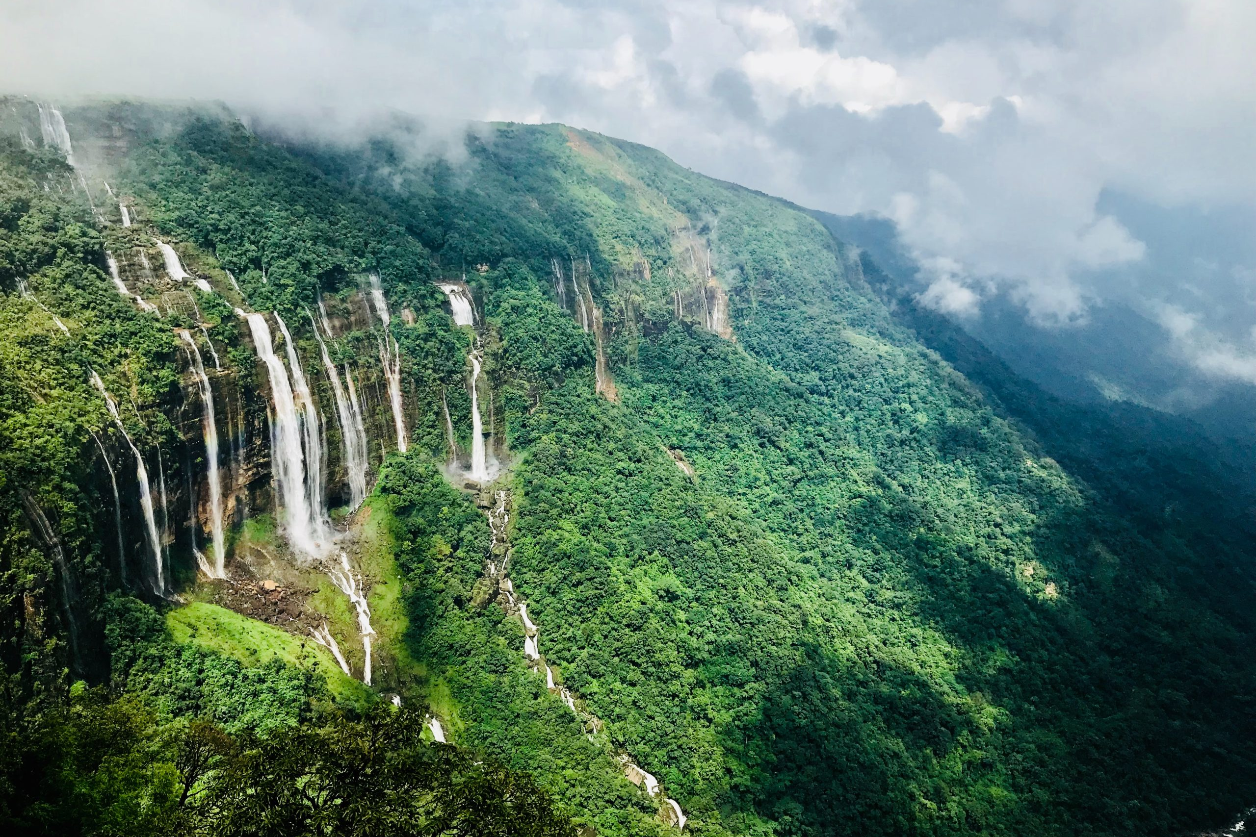 Seven parallel waterfalls cascading down a lush green cliff in meghalaya.