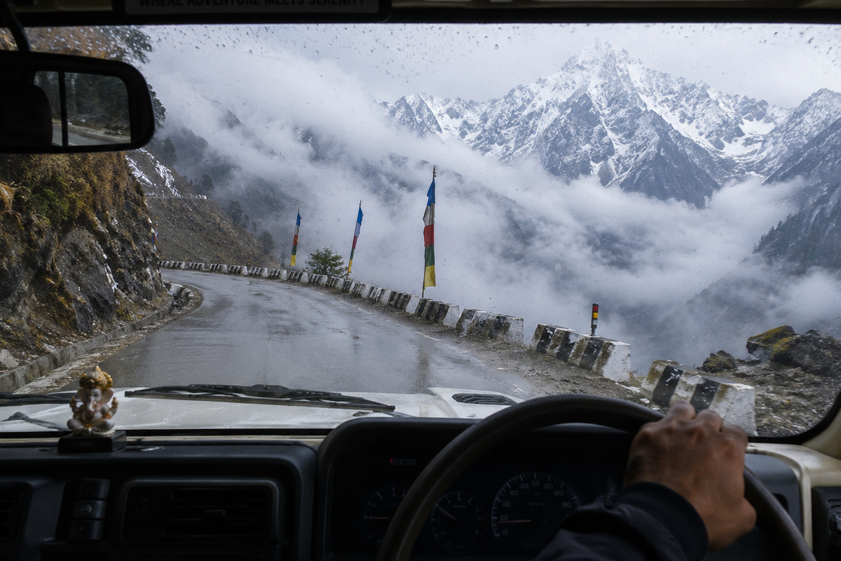 "A first-person view from inside a 4x4 vehicle driving on a winding, misty mountain road in North Sikkim with snow-capped peaks in the background."
