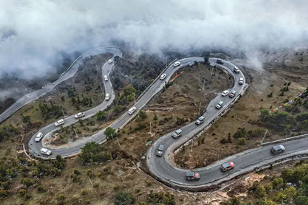 A private white SUV driving through the scenic, winding mountain roads of Arunachal Pradesh.