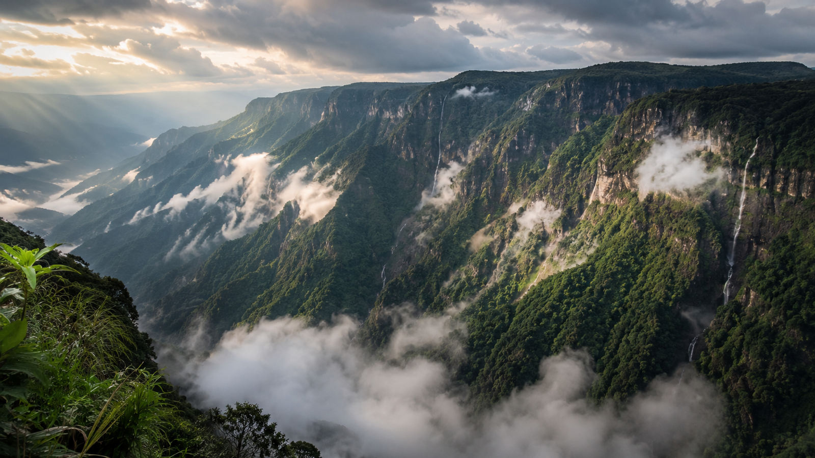 A cinematic panoramic view of a deep mountain gorge in Cherrapunji, Meghalaya, with dramatic mists and clouds parting over emerald-green cliffs."