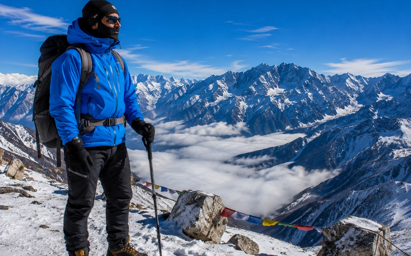 A traveler fully equipped in high-altitude technical winter wear standing safely beside a snowy ridge overlook at Sela Pass."