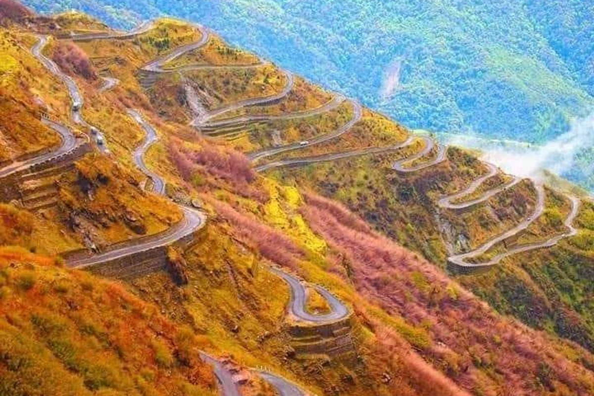 A panoramic view of the winding Zig-Zag roads of Zuluk in East Sikkim under a soft golden morning light.