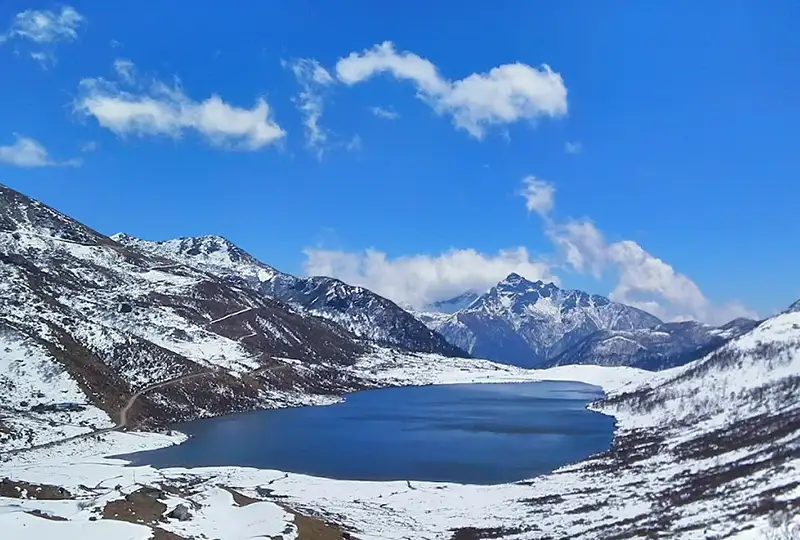 Oval glacial Tsomgo Changu Lake in Sikkim with colorful prayer flags and snow-capped mountains.