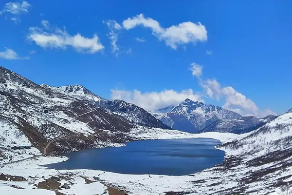Oval glacial Tsomgo Changu Lake in Sikkim with colorful prayer flags and snow-capped mountains.