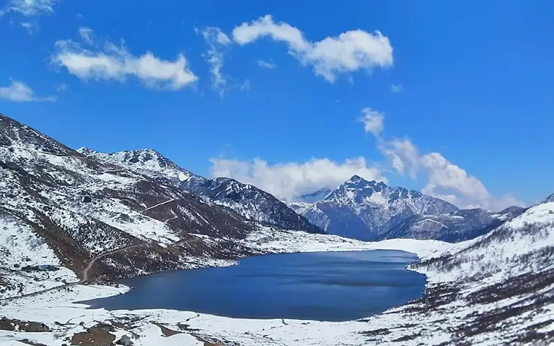Oval glacial Tsomgo Changu Lake in Sikkim with colorful prayer flags and snow-capped mountains.