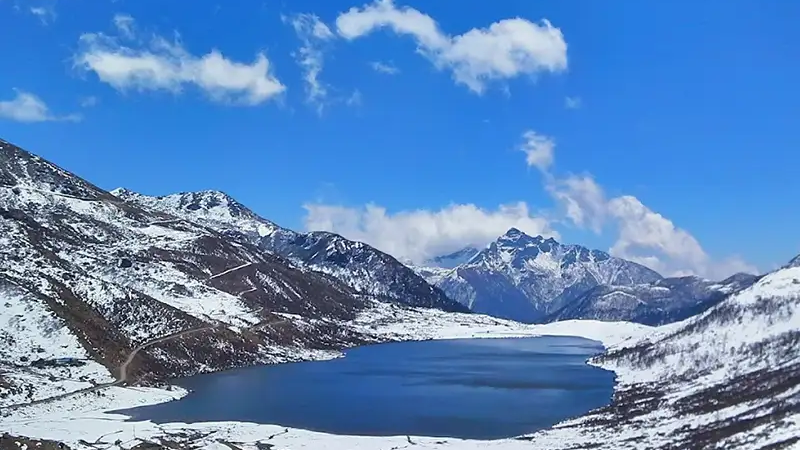 Oval glacial Tsomgo Changu Lake in Sikkim with colorful prayer flags and snow-capped mountains.
