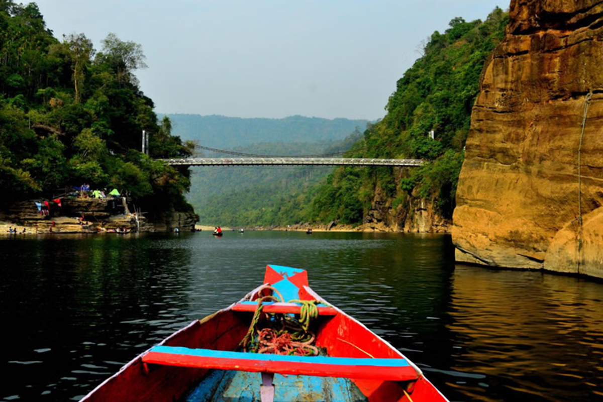 A traditional wooden country boat floating on the crystal clear turquoise water of the Umngot River in Dawki Meghalaya under a clear sky
