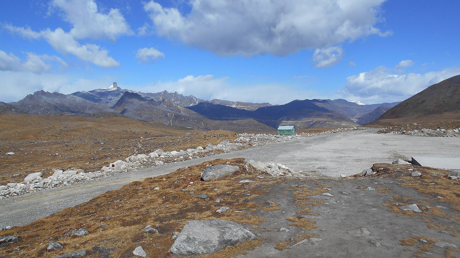 The wide, barren Bum La Pass at the India–China border with brown hills and snow peaks under a blue sky