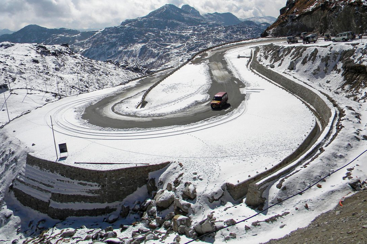 A wide-angle panoramic view of the winding mountain roads leading to Nathu La Pass in East Sikkim, shrouded in clouds.