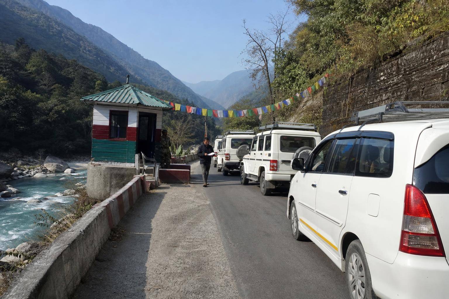 A line of white taxis waiting at a small police checkpost beside a turquoise mountain river in Sikkim