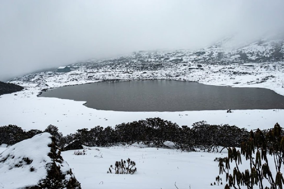 Completely frozen surface of Sangetsar Lake with dead trees and snow-capped peaks in February.