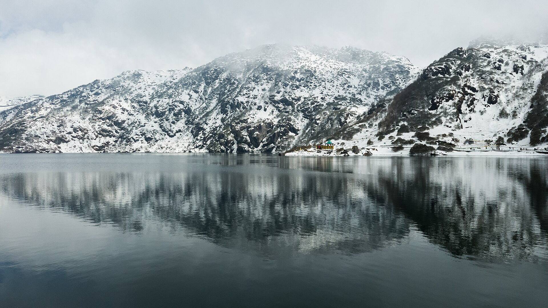 Tsomgo Lake in East Sikkim with snow on the surrounding mountains and their reflection in the still water