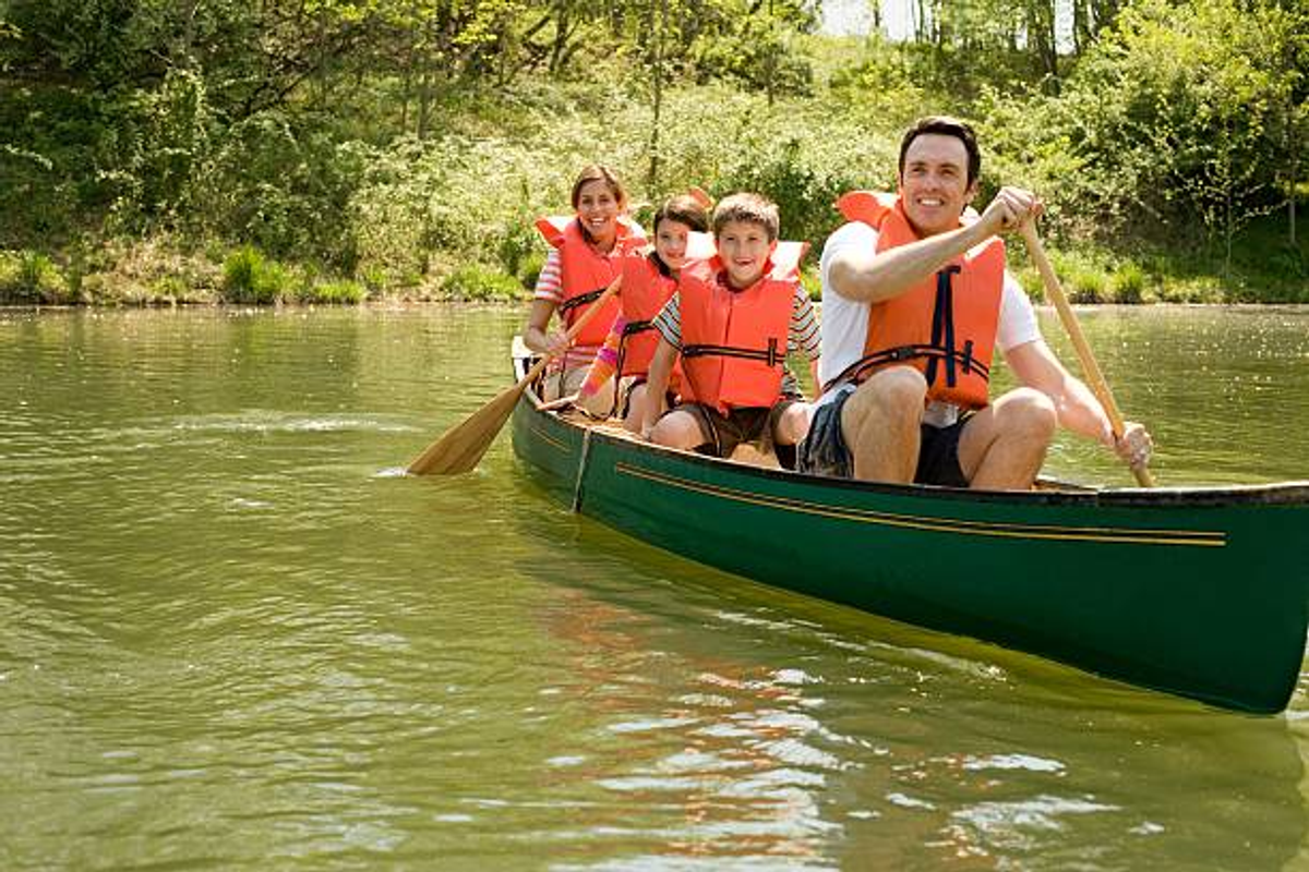 Travelers wearing orange life jackets sitting inside a long wooden canoe inside a narrow rock gorge.